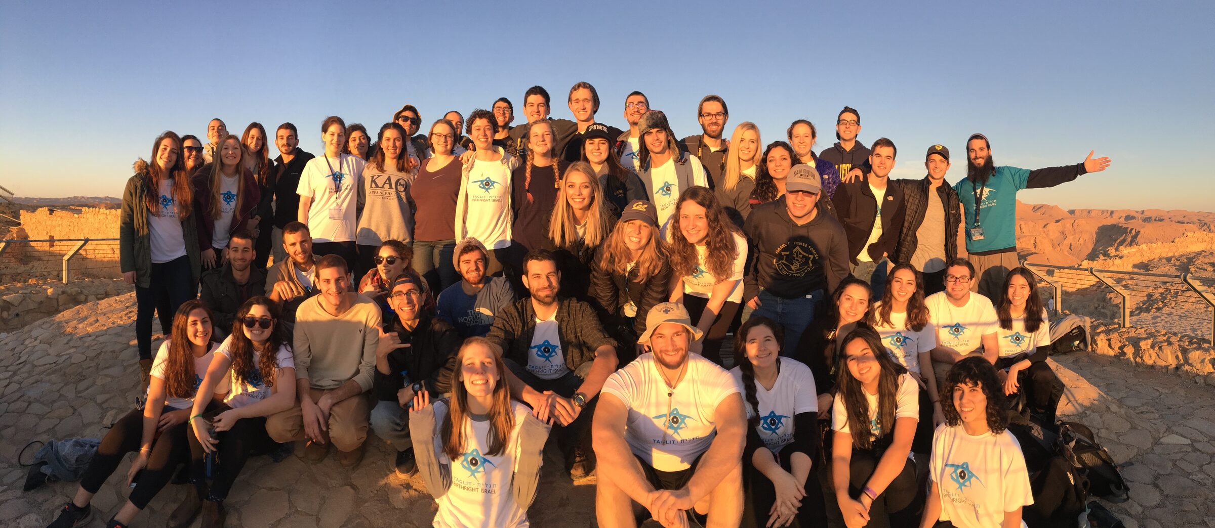 A large group of students gathered on a desert overlook at golden hour