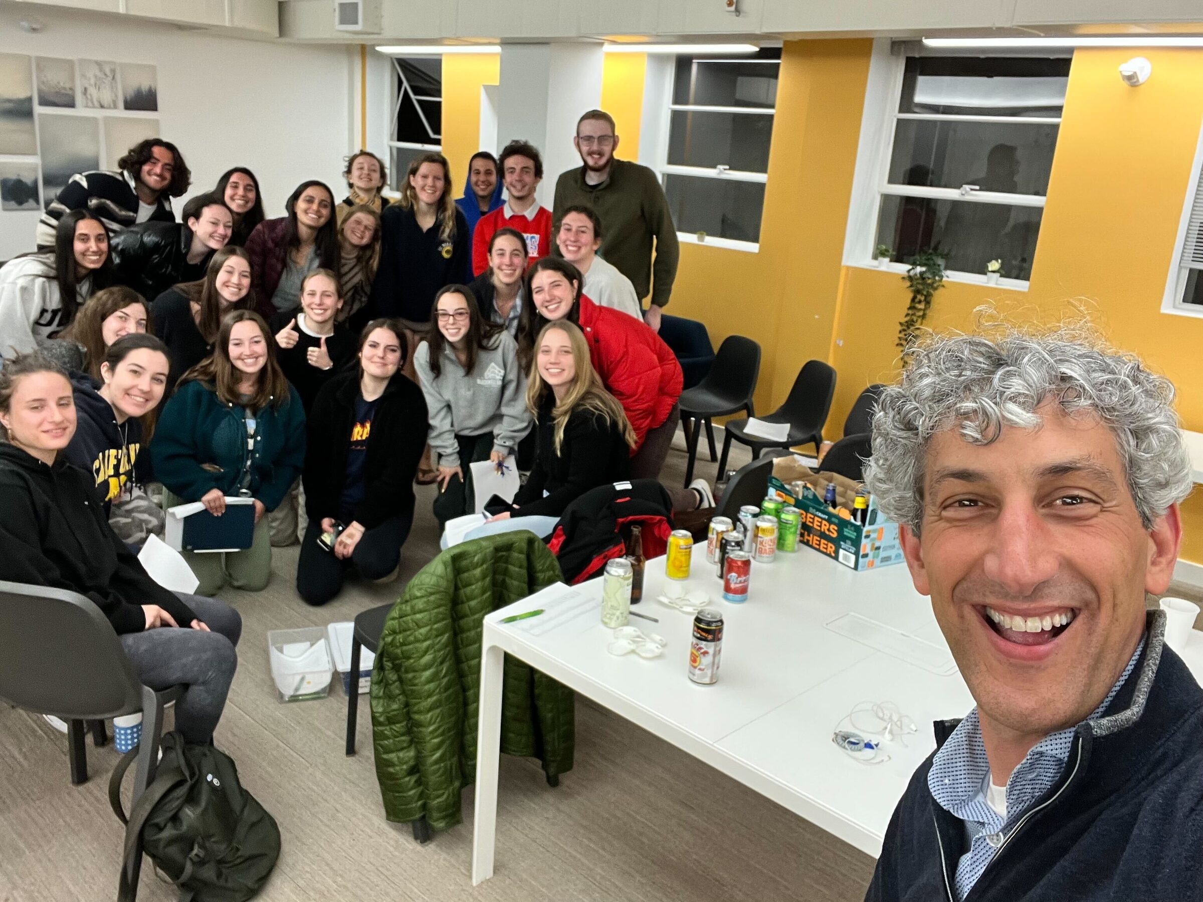 A crowded room of students gathered around a table of drinks and snacks