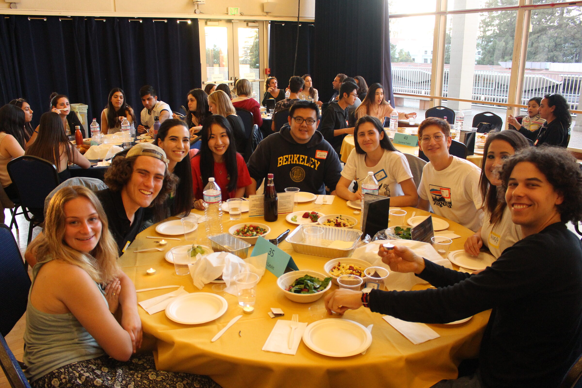 Students around a round table set for Shabbat dinner, turning to smile at the camera